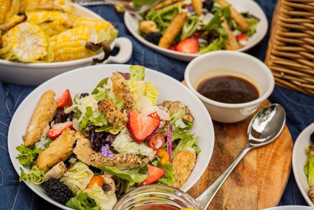 Green salad topped with Hungry Planet grilled chicken and berries, with a dish of balsamic dressing on the side