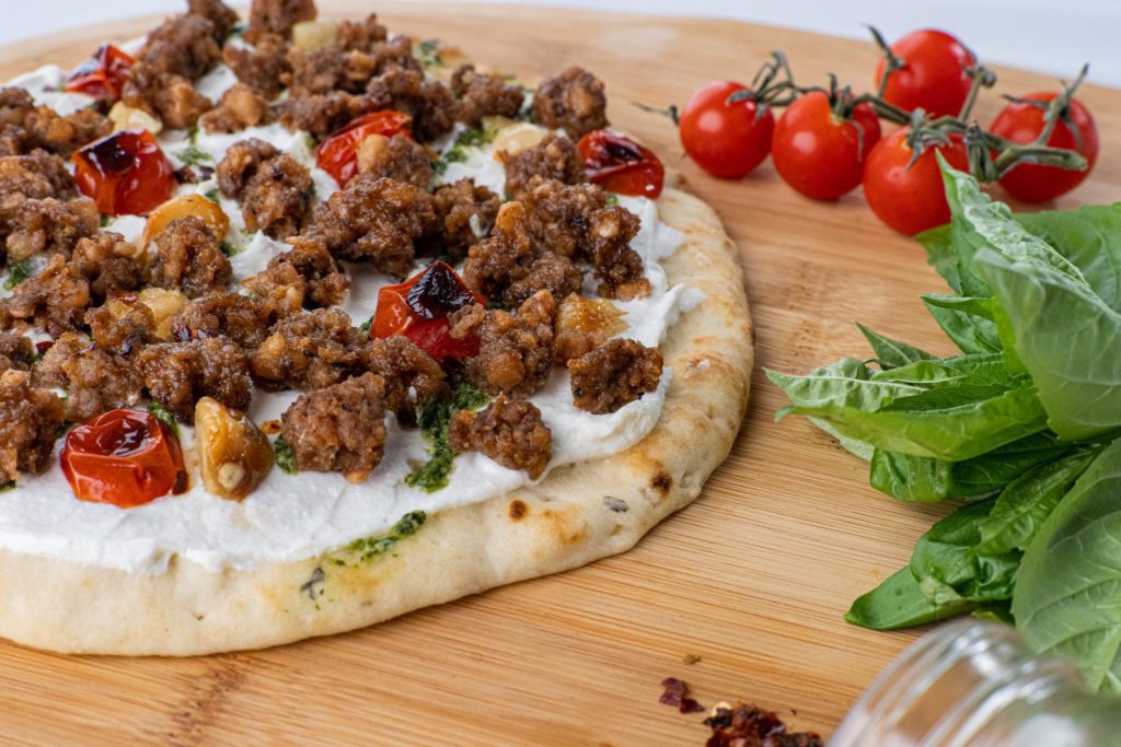 Pizza topped with Hungry Planet Italian sausage, ricotta cheese, and roasted cherry tomatoes and garlic