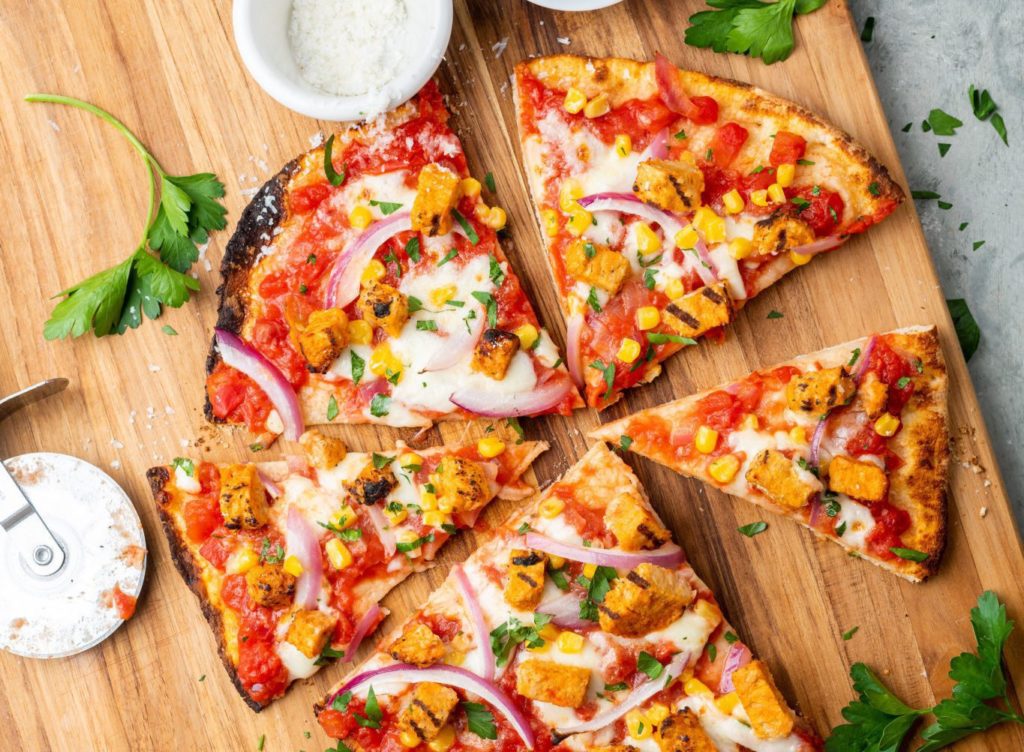 Pizza topped with Hungry Planet grilled chicken, mozzarella, onions, corn, and cilantro cut into triangular slices