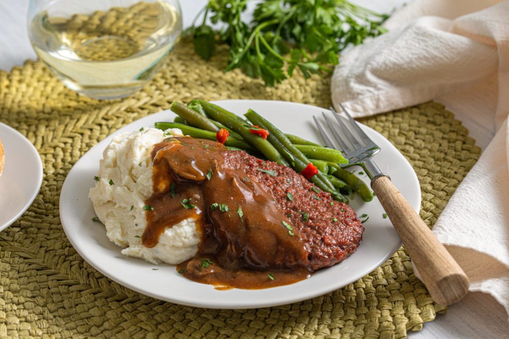 Hungry Planet Salisbury steak topped with mushroom gravy on a plate with mashed potatoes and green beans
